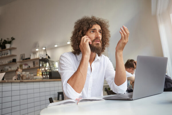 Ein Mann macht eine Handbewegung, während er ein ernstes Gespräch am Telefon führt (Ombudsdienst für Telekommunikation).