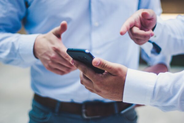 Een persoon die iets op zijn smartphone toont aan een andere persoon (Ombudsdienst voor telecommunicatie).