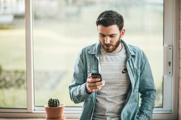 A man leaning back against a window, looking at his telephone A man leaning back against a window, looking at his telephone (Office of the Ombudsman for Telecommunications).